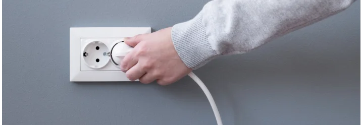 Eine Person zieht den Stecker aus der Steckdose.